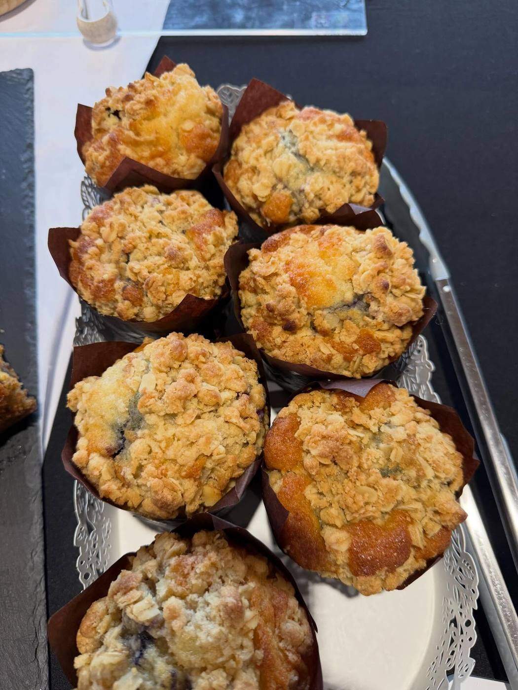 Blueberry streusel muffins in brown paper cases, dusted with streusel topping, on a slate presentation tray