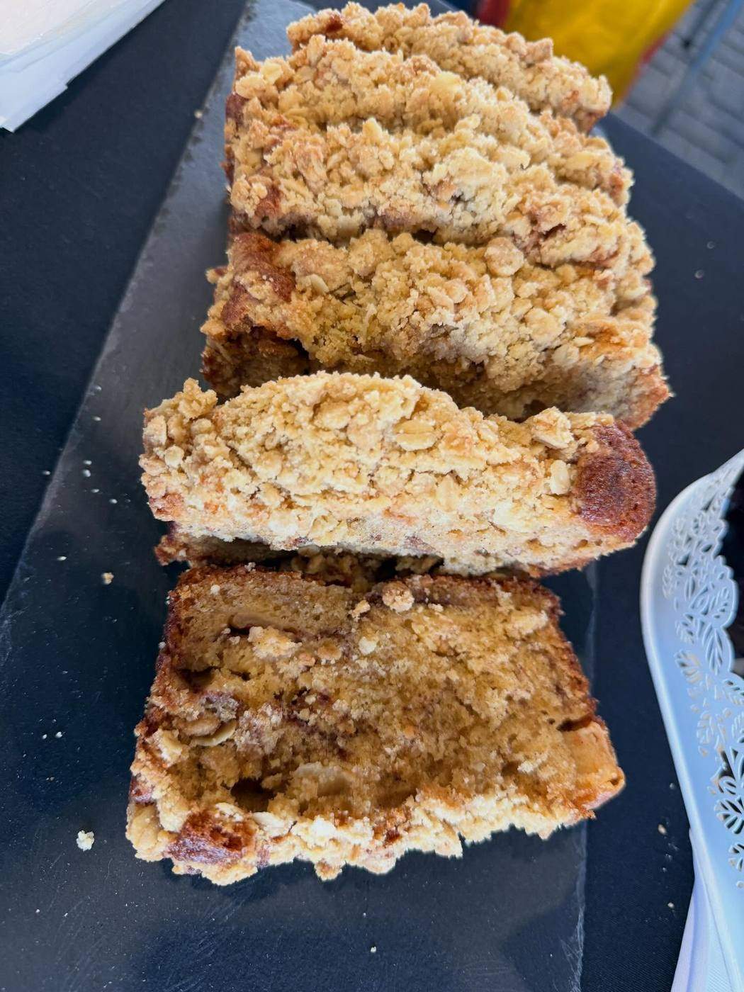 Slices of crumb-topped apple and cinnamon loaf cake on a slate market plate